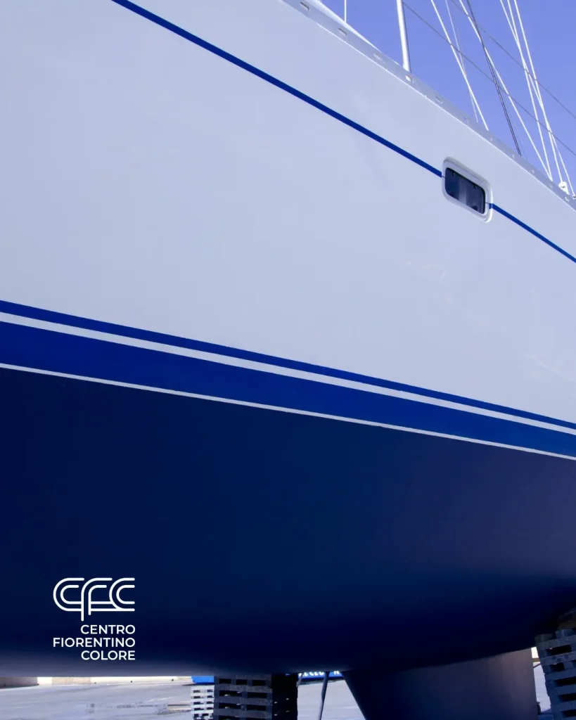 CFC Nautica e Yachting 1 CFC - Nautica e Yachting - Close-up of a yacht's hull showing white and blue paint with lines and a small window.